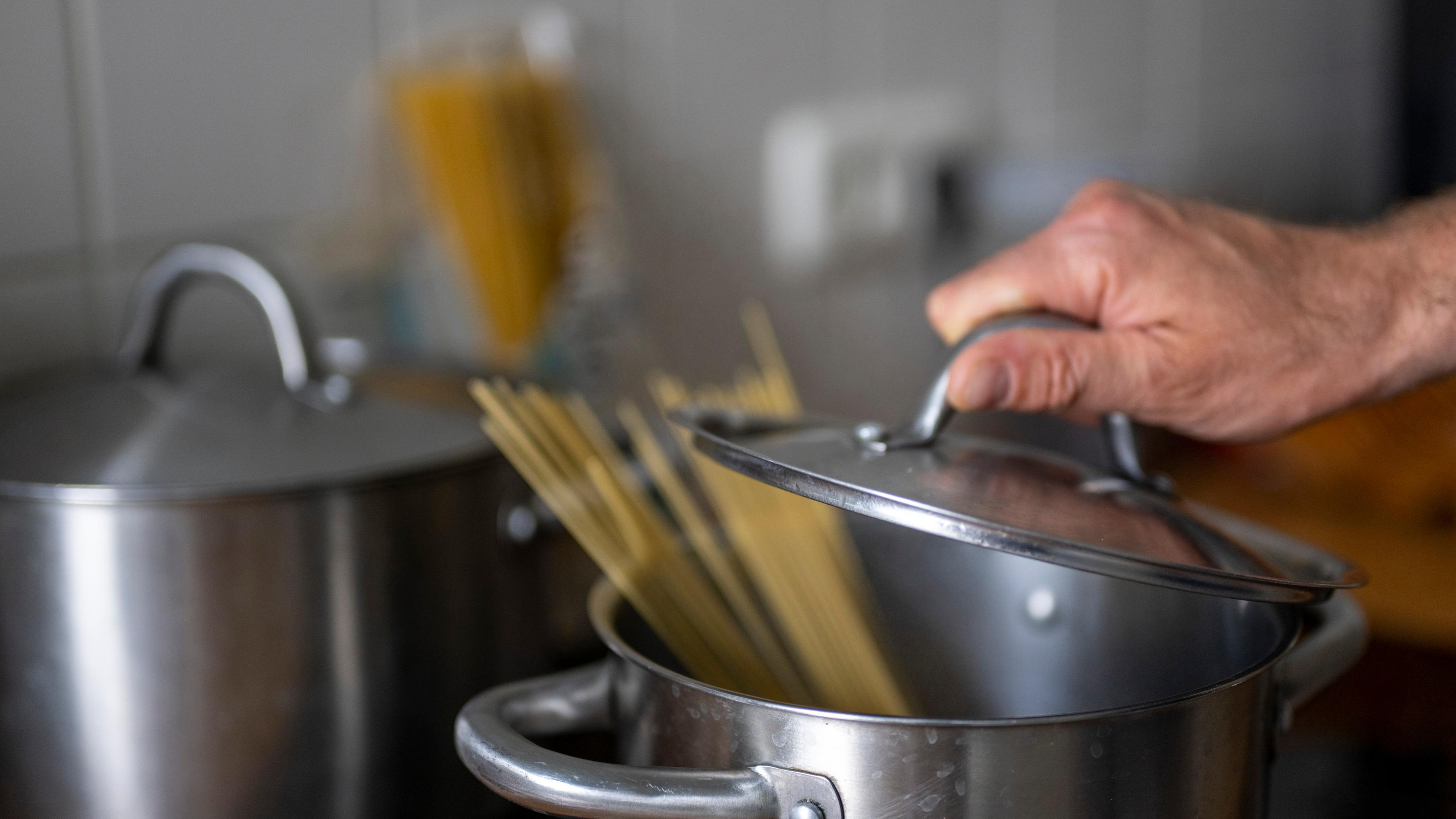 Ein Mann legt einen Deckel auf einen Topf mit kochendem Wasser und Spaghetti-Nudeln. 