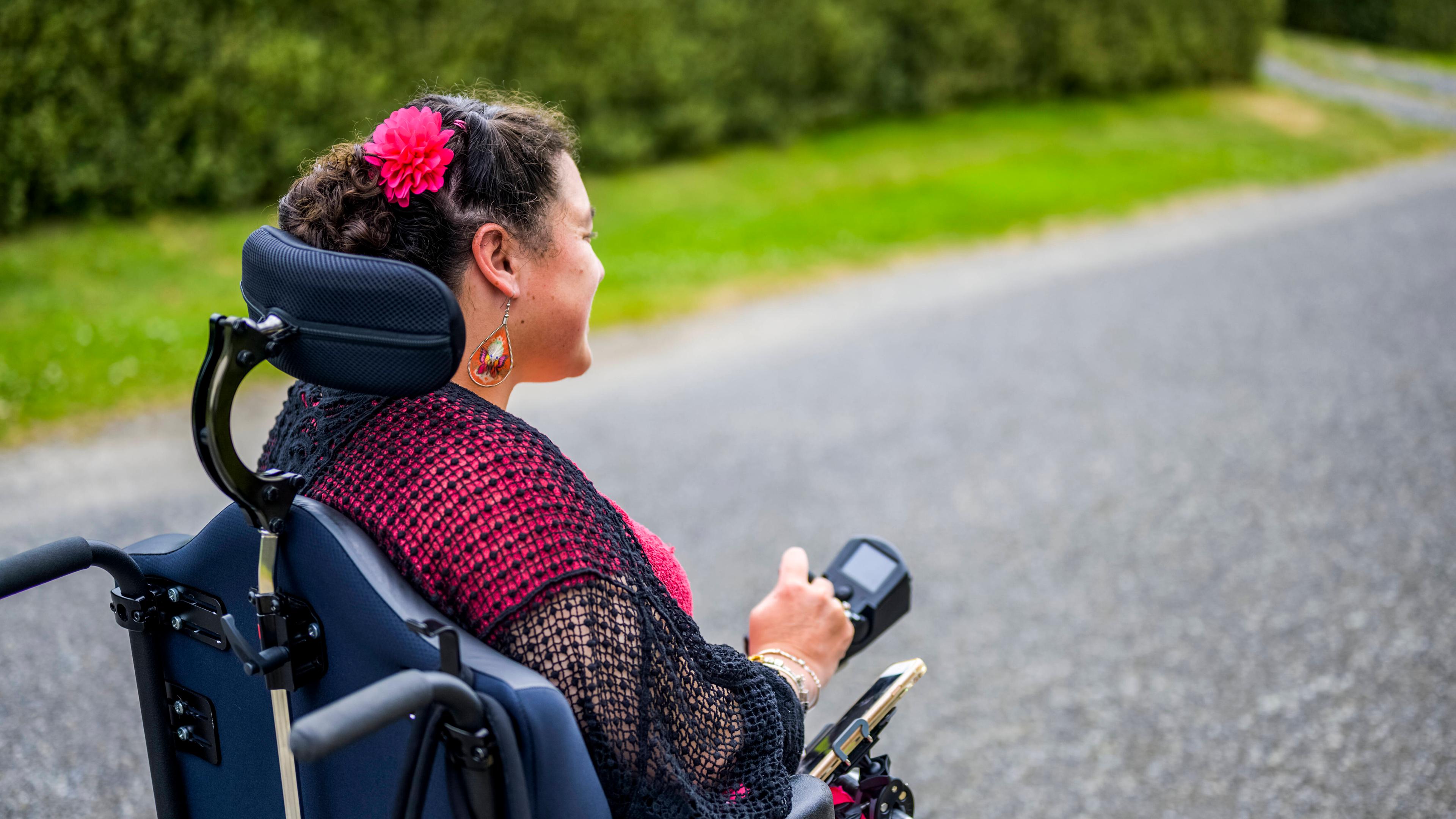 Frau sitzt im Rollstuhl und fährt auf Straße
