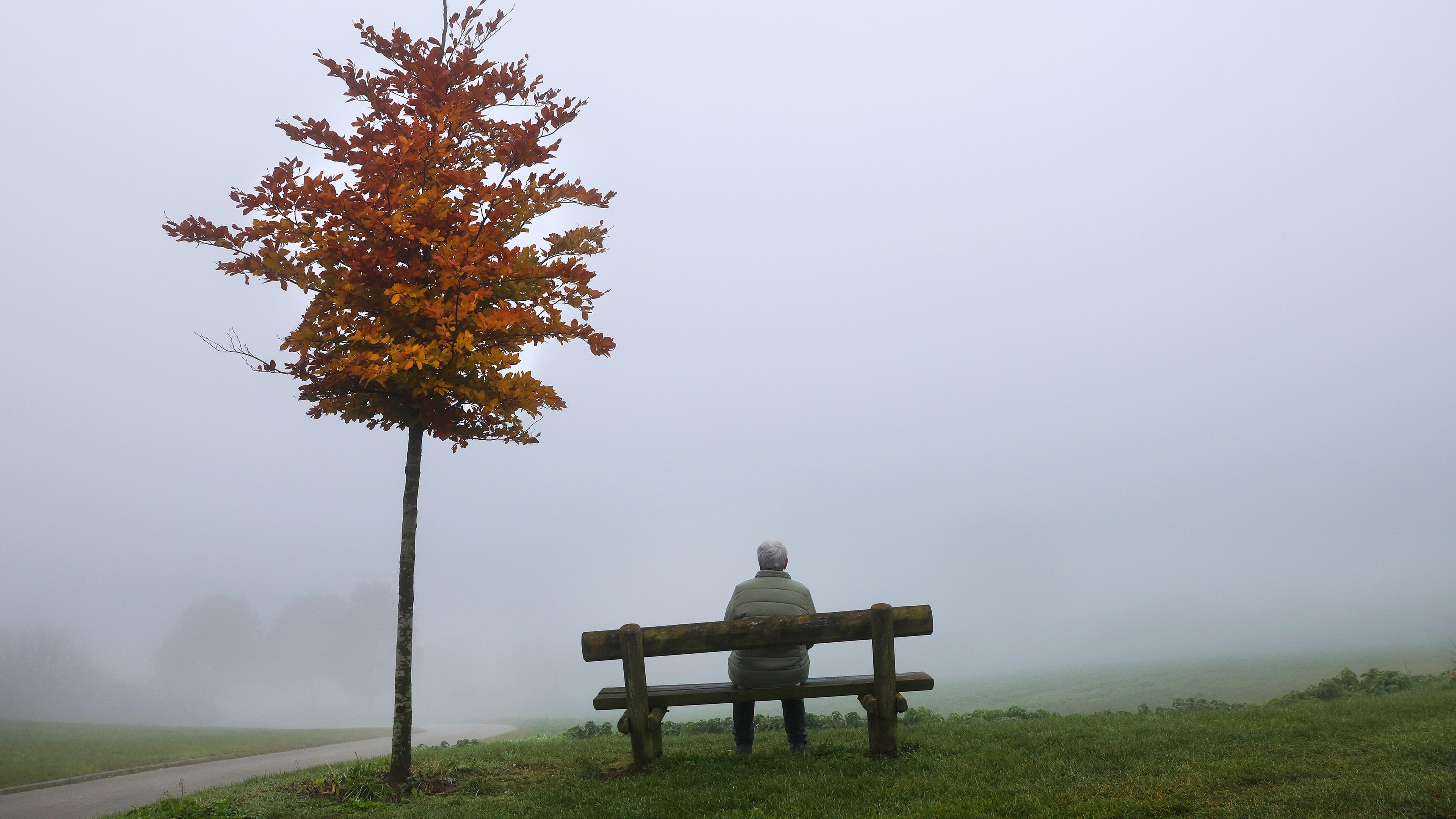 Eine Frau sitzt im Nebel auf einer Bank.