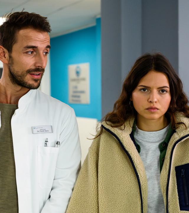 "Bettys Diagnose - Einsichten": Dr. Frank Stern (Max Alberti) und Emily Hansen (Nina Kaiser) stehen auf den Krankenhausflur. Er dreht sich zu ihr und redet mit ihr. Sie schaut genervt.