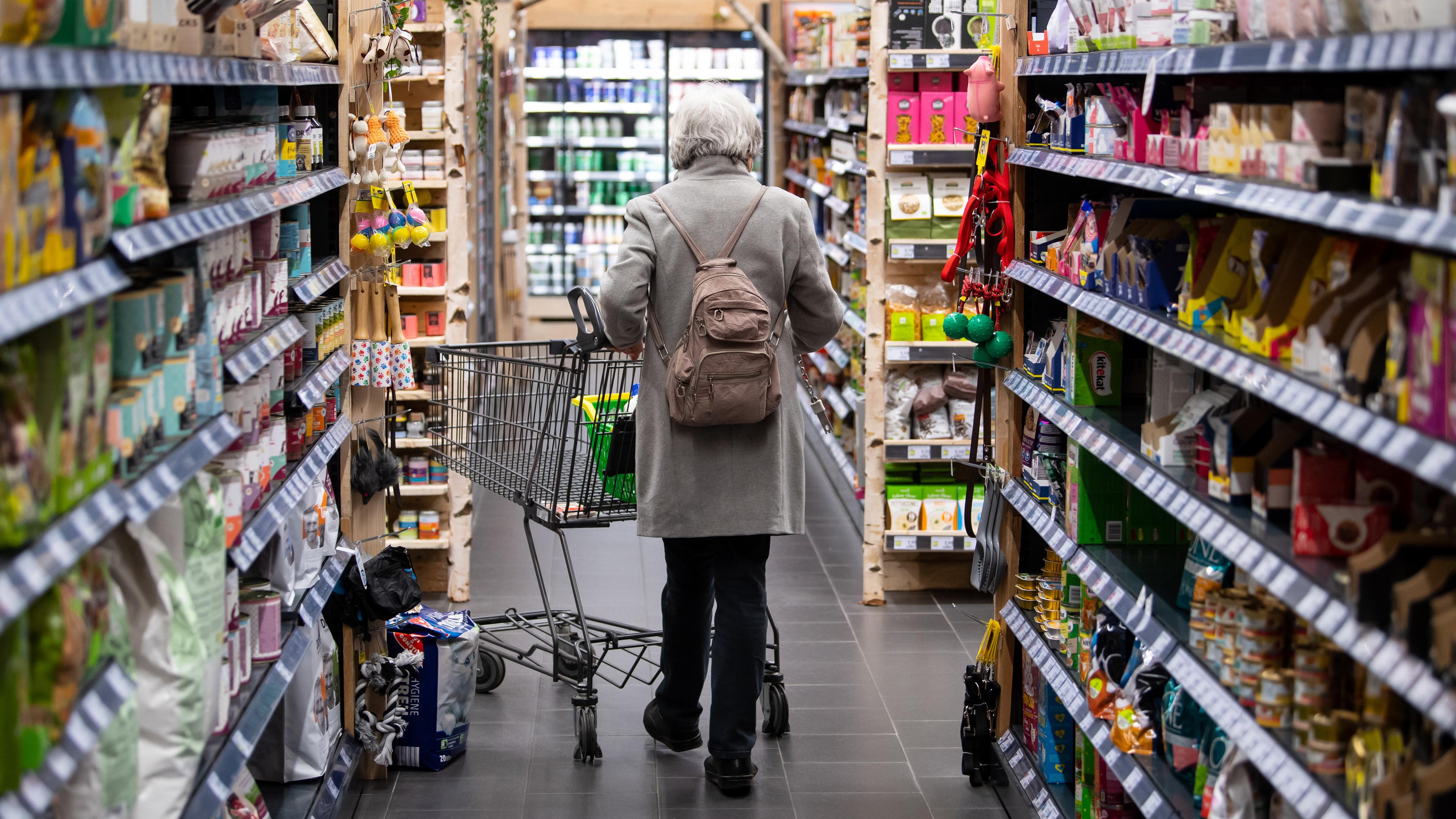 Eine Frau geht mit ihrem Einkaufswagen durch einen Supermarkt. 