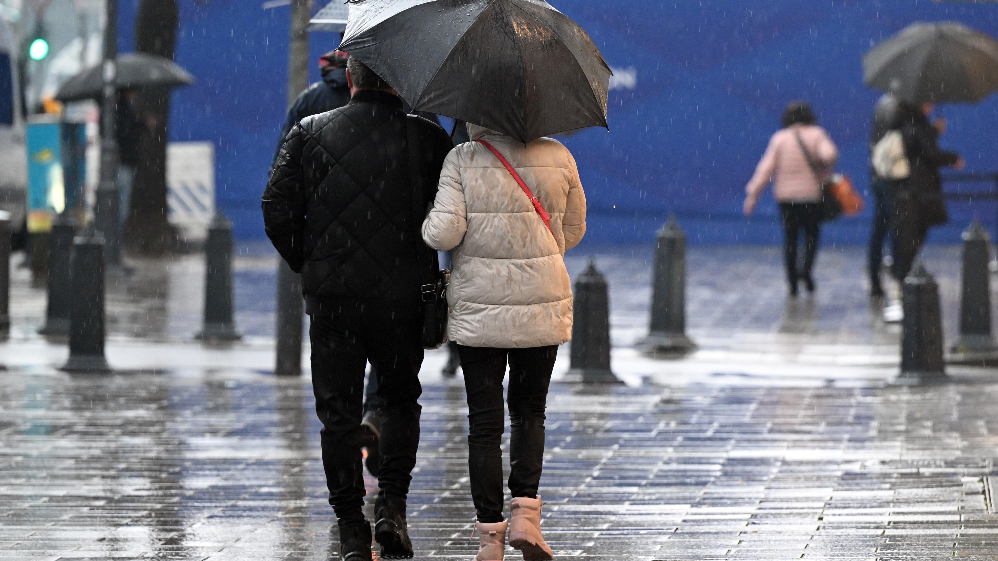 Passanten gehen unter ihrem Regenschirm über die Königsallee. 