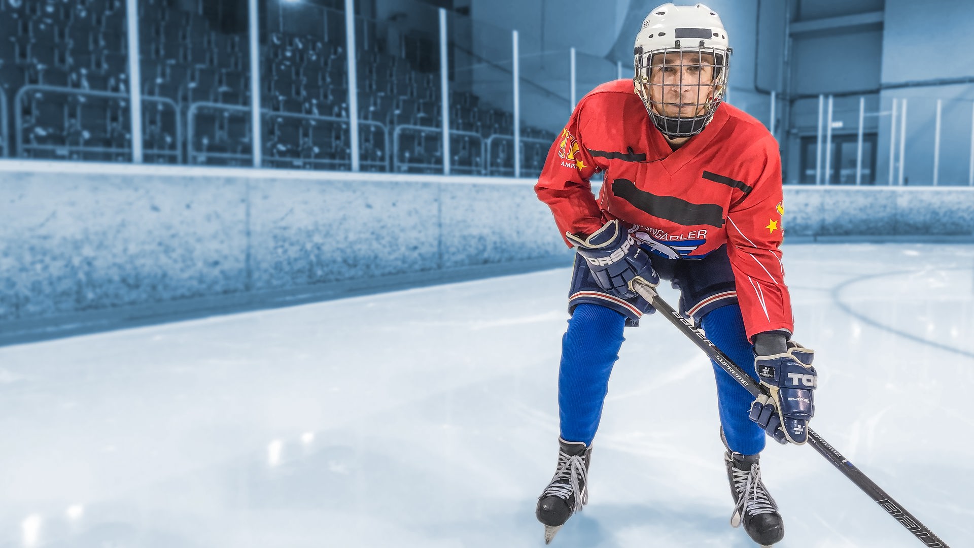 Eric Mayer steht im voller Eishockey-Ausrüstung auf Kufen auf dem Eis und hält auch einen Eishockeyschläger in den Händen. 