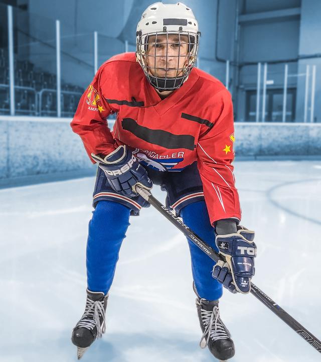 Eric Mayer steht im voller Eishockey-Ausrüstung auf Kufen auf dem Eis und hält auch einen Eishockeyschläger in den Händen. 