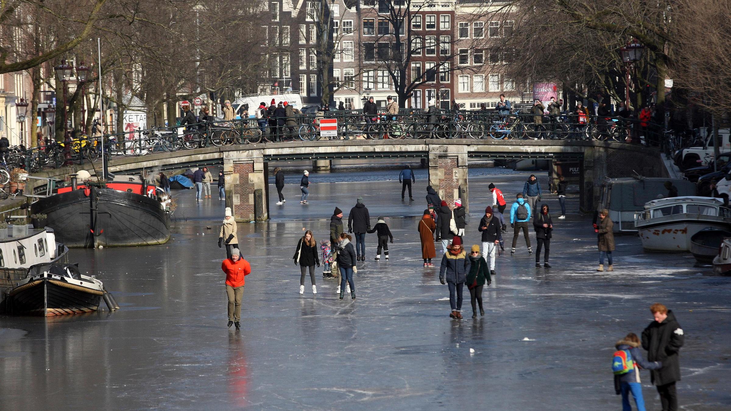 Menschen gehen auf den Kanälen in Amsterdam Eislaufen.