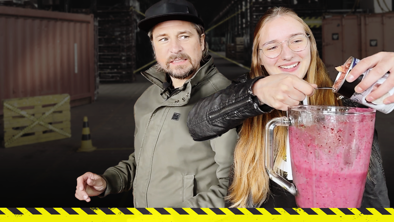 Checkpoint: Moderator Tommy Scheel schaut leicht angeekelt und skeptisch Testteamerin Laura zu, wie sie Hundefutter in einen Smoothie kippt. 