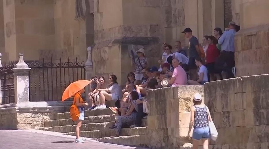 Eine Gruppe von Menschen sitzt im Schatten während eine Frau mit einem Regenschirm sich von der Sonne schützt