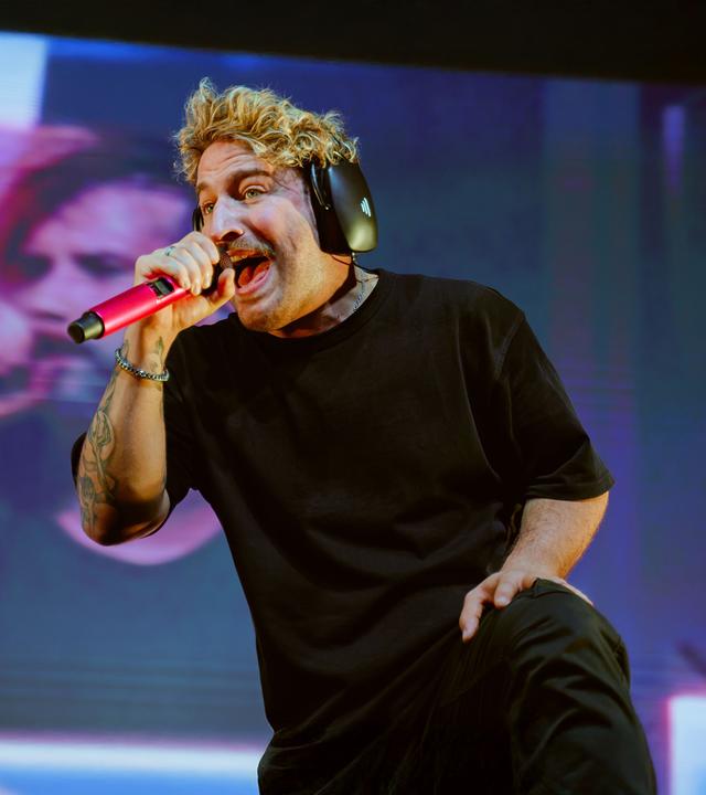 Electric Callboy-Sänger Nico Sallach ist auf der Bühne und singt in ein rosa Mikrofon.