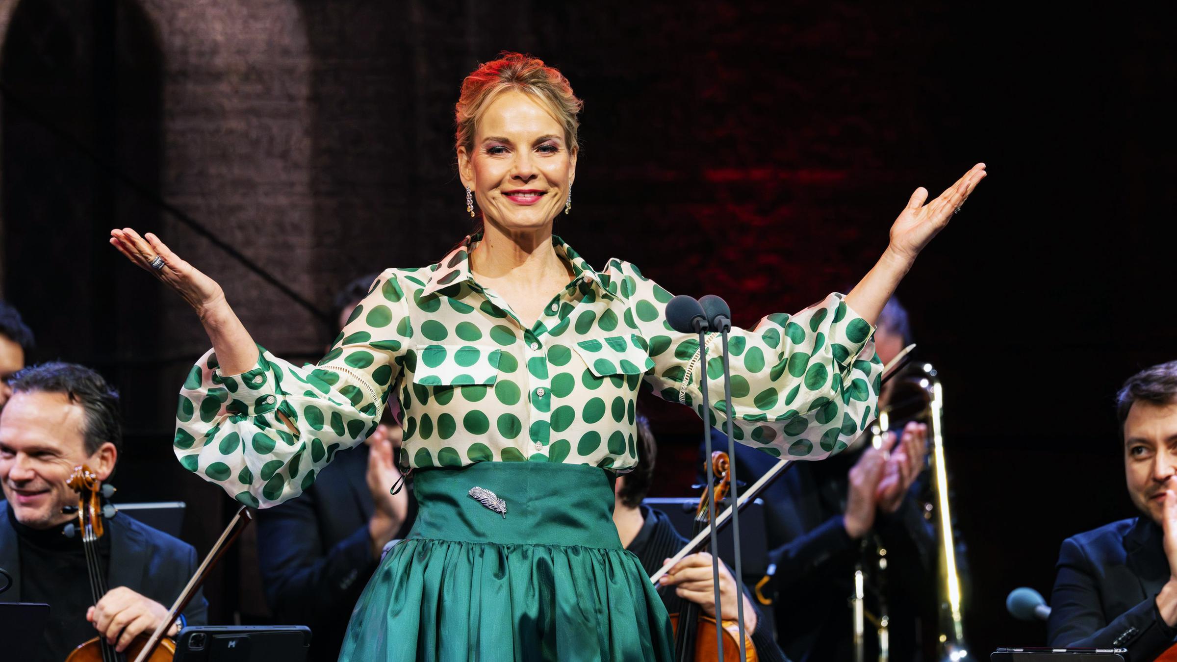 Sängerin Elīna Garanča im grüner Festkleidung und ausgebreiteten Armen