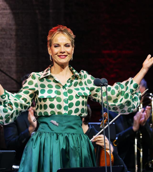 Sängerin Elīna Garanča im grüner Festkleidung und ausgebreiteten Armen