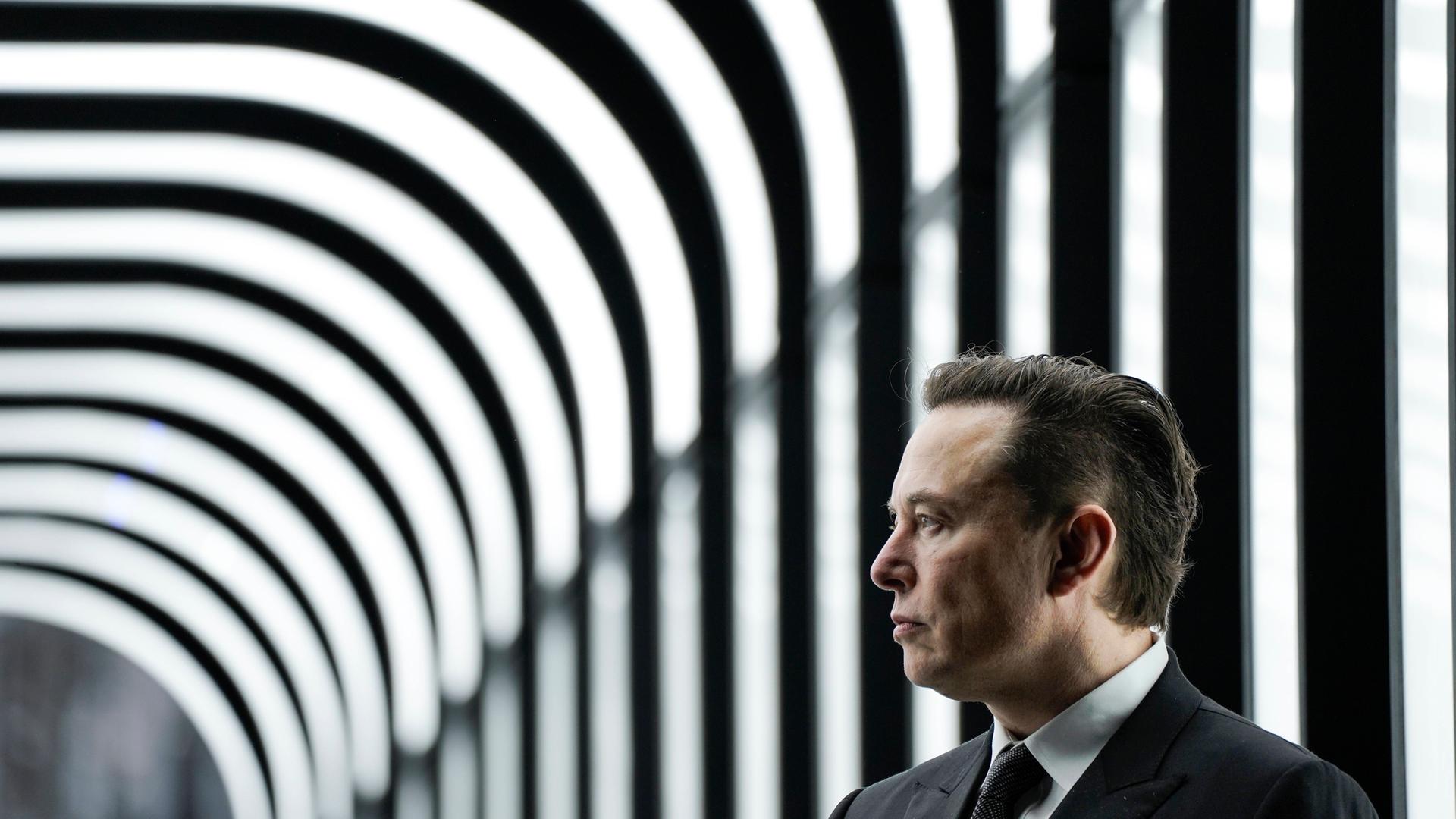 Ein Mann mittleren Alters im grauen Anzug steht vor einem schwarz-weiß-gestreiften Hintergrund.