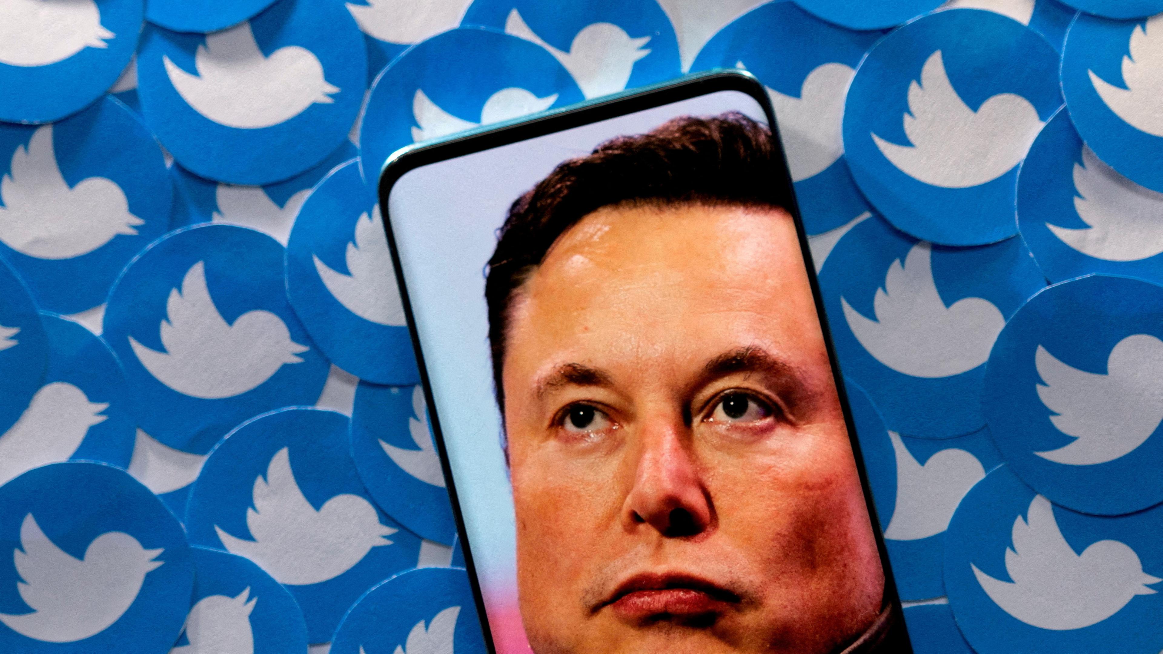 Das Konterfei Elon Musks auf einem Handy, dahinter zahlreiche Twitter-Symbole.