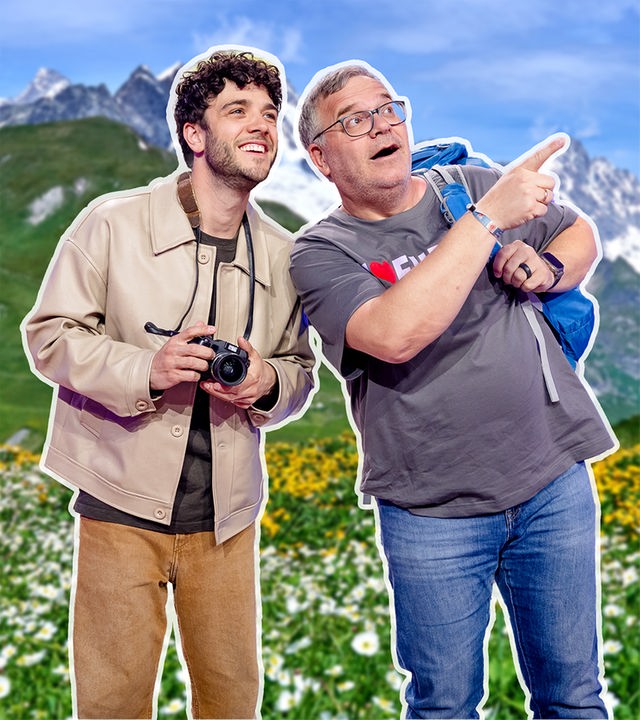 Vor einer alpinen Kulisse mit Wiesen und Bergen schauen Luca Hänni und Elton nach oben. Elton deutet mit dem Finger auf etwas in der Ferne.