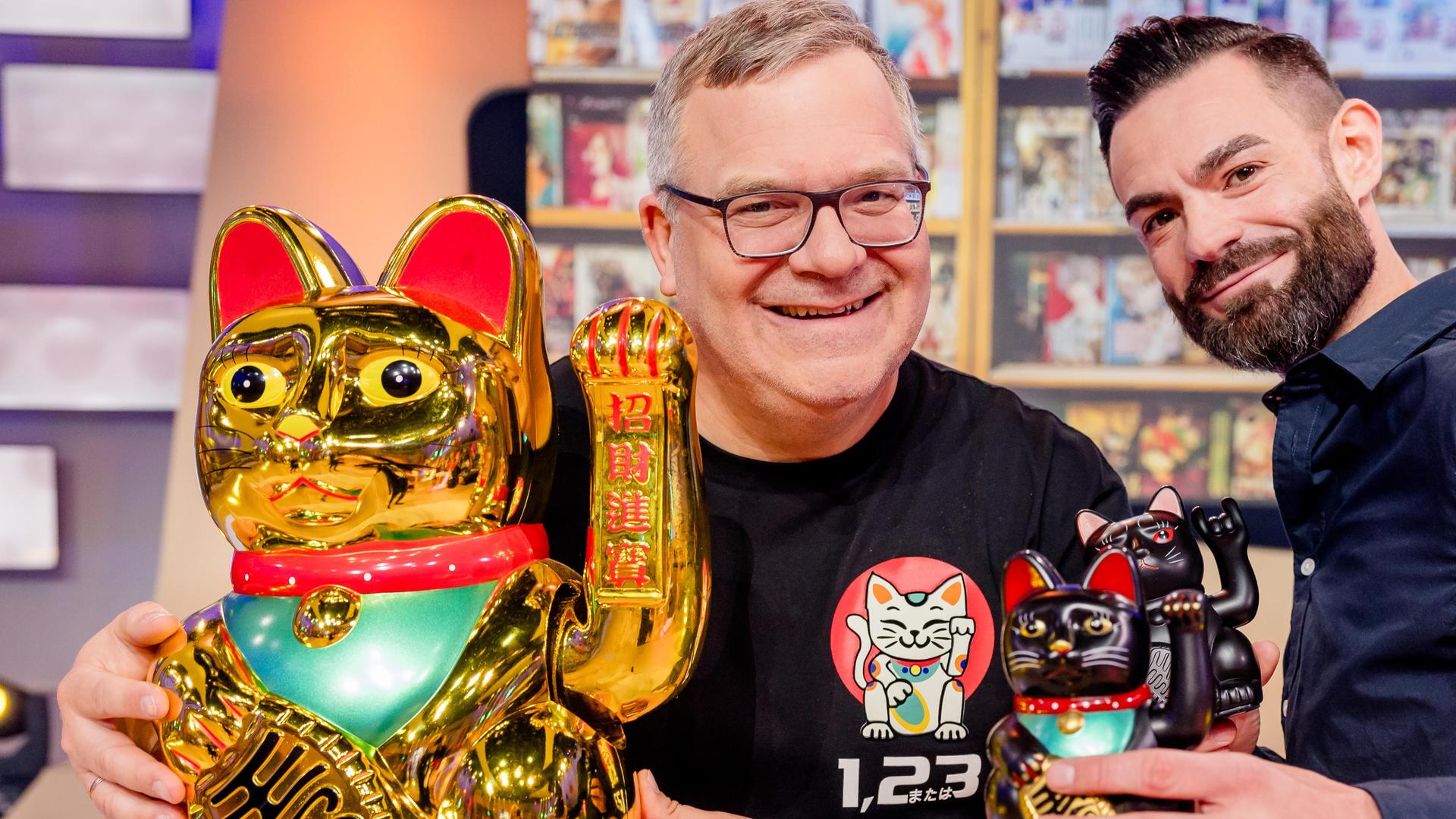Manga-Experte Nino Kerl (r.) und Elton halten Winkekatzen in unterschiedlicher Größer.