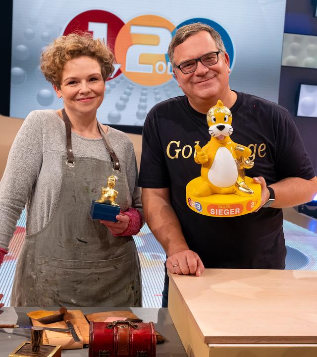 Expertin Bettina Siegmund-Felber steht neben Elton. Dieser hält einer Figur von Piet Flosse in der Hand.