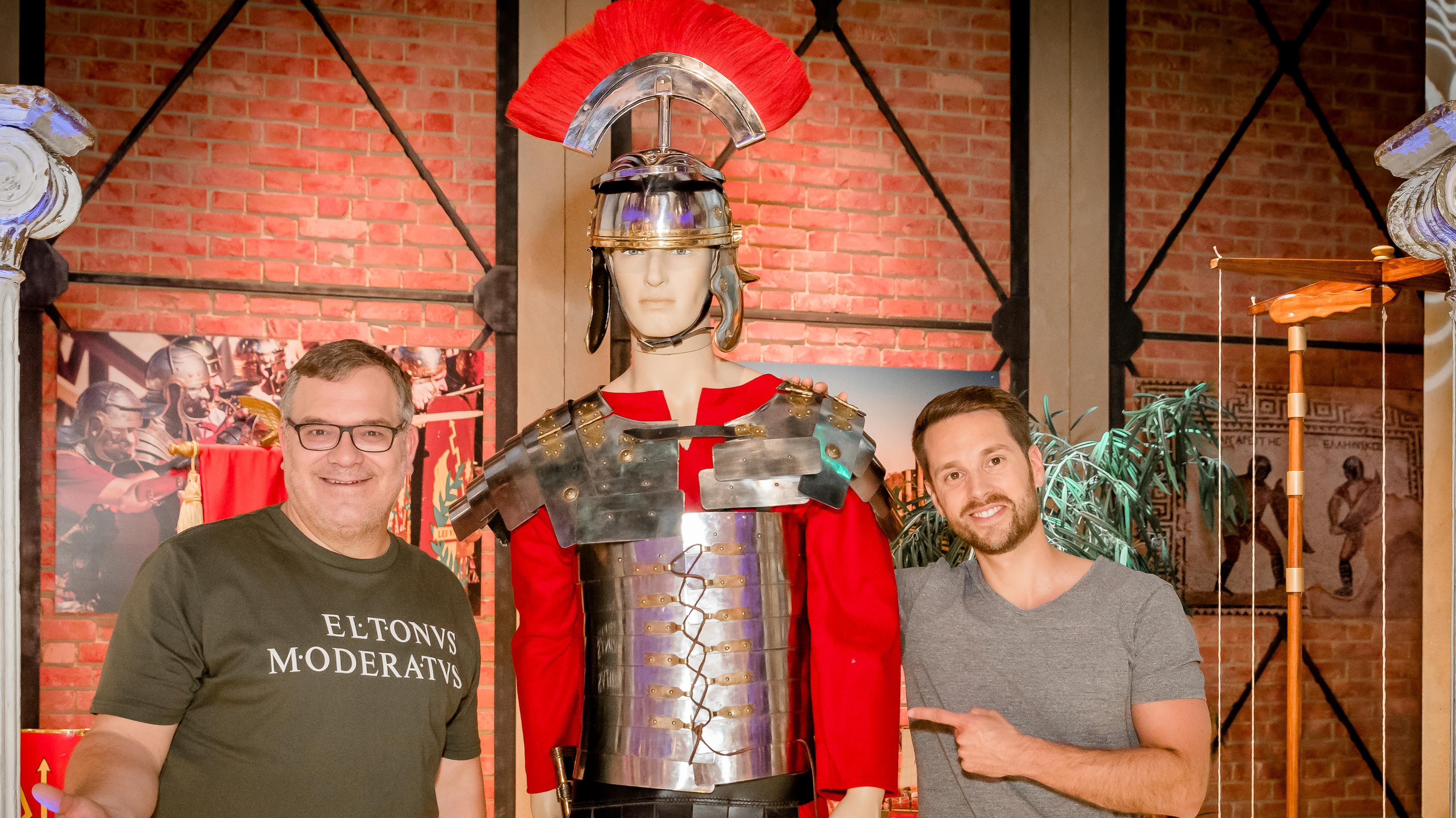 1, 2 oder 3: Moderator Elton steht mit dem Studiogast im 1, 2 oder 3-Studio und schaut erfreut in die Kamera. Beide zeigen auf eine Figur mit einer römischen Rüstung.