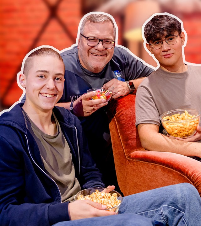 Vico und Dominik sitzen auf Sesseln und lächeln. Elton kniet dahinter und lächelt.