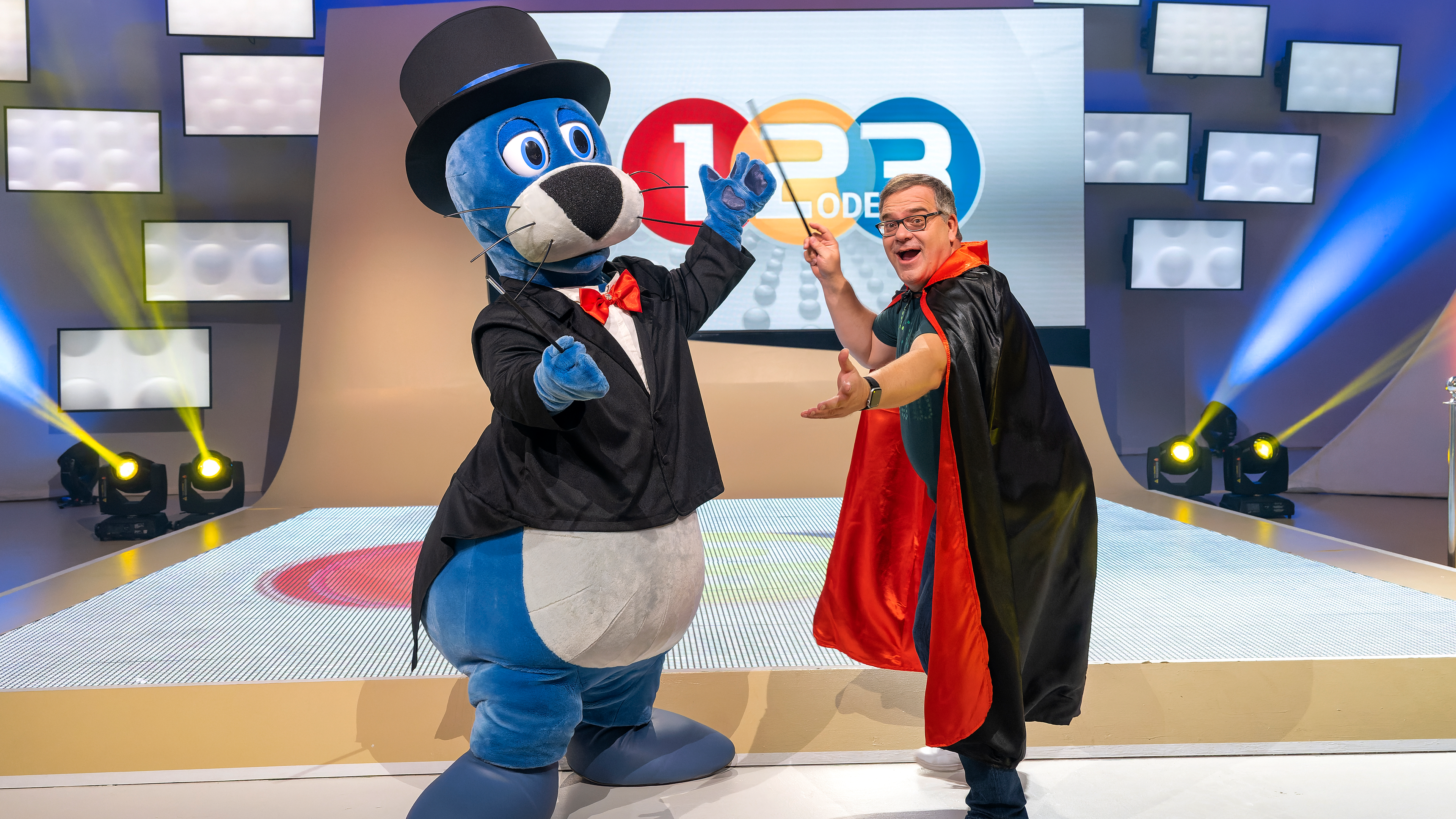 Elton trägt ein Zauberumhang und in seiner rechten Hand schwingt er einen Zauberstab. Piet Flosse trägt ein Kostum und einen Zylinder.