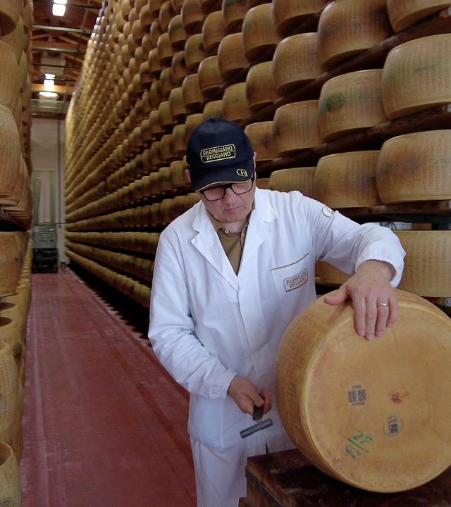 Mann mit großem Käserad vor Regalen voller Käseräder.