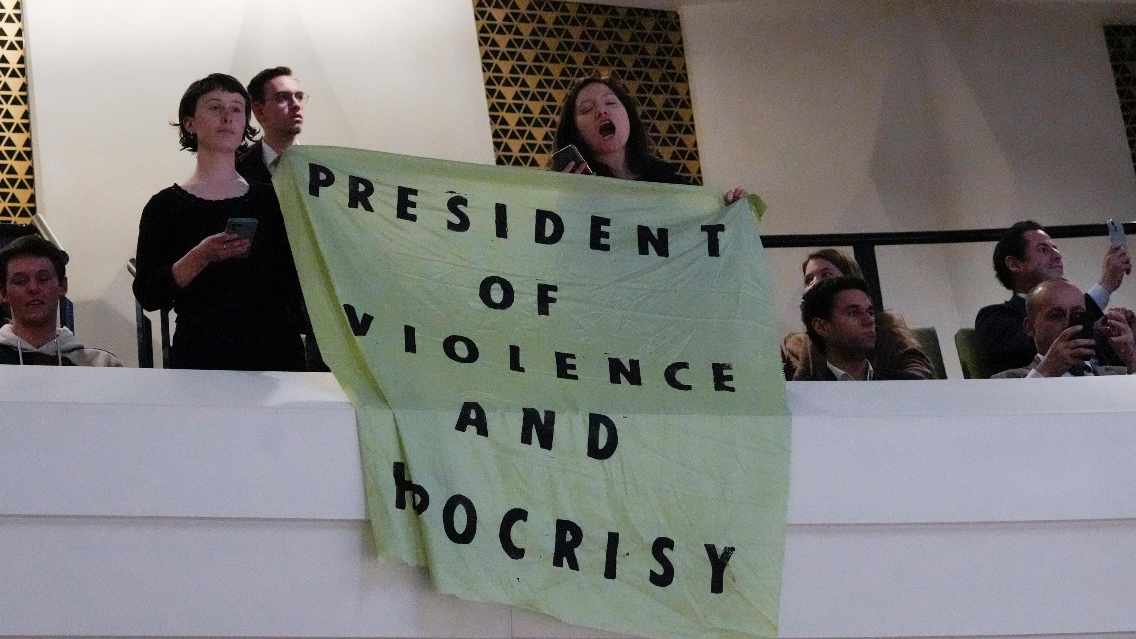 Niederlande, Den Haag: Demonstranten halten ein Transparent mit der Aufschrift "Präsident der Gewalt und der Heuchelei" hoch, während der französische Präsident Macron in einem Theater seine Vision von der Zukunft Europas erläutert.