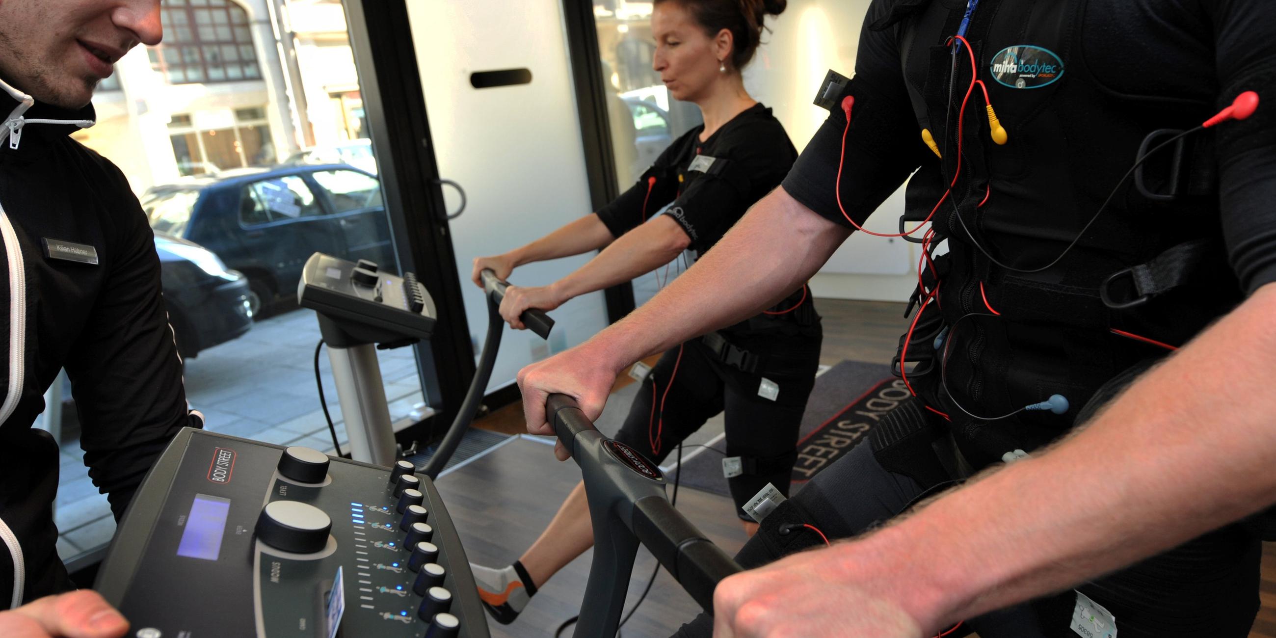 Zwei Personen mit Weste und Elektroden werden beim EMS-Training im Fitnesstudio angeleitet.