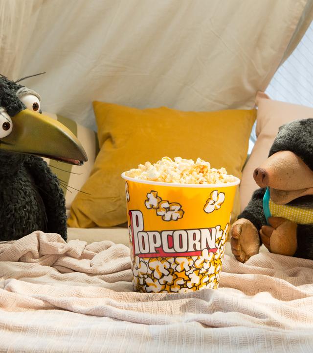 Rudi und Grete hocken in der Kuschelecke und schauen begierig auf einen Eimer voller Popcorn.