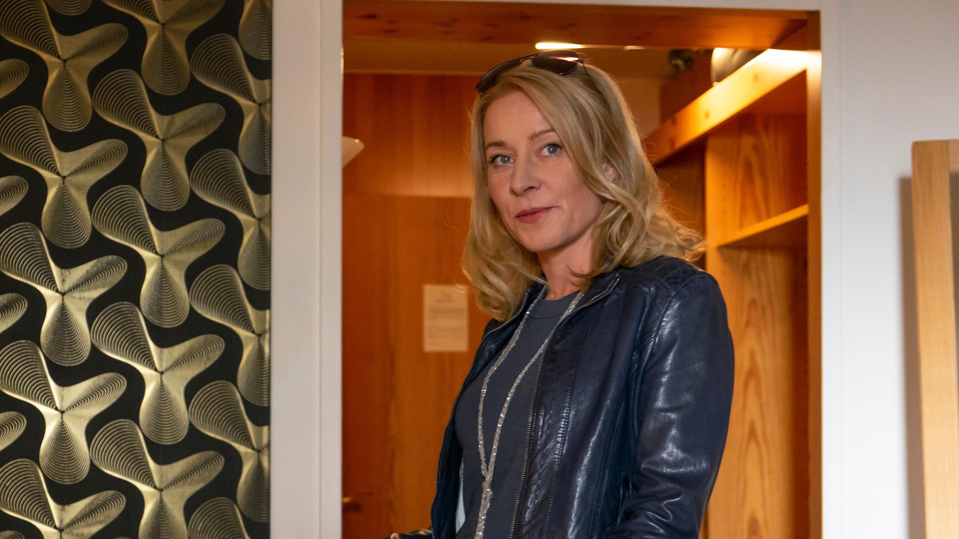 Susanne (Natalie O'Hara) steht im neuen schwarzen Outfit im Hotelzimmer.