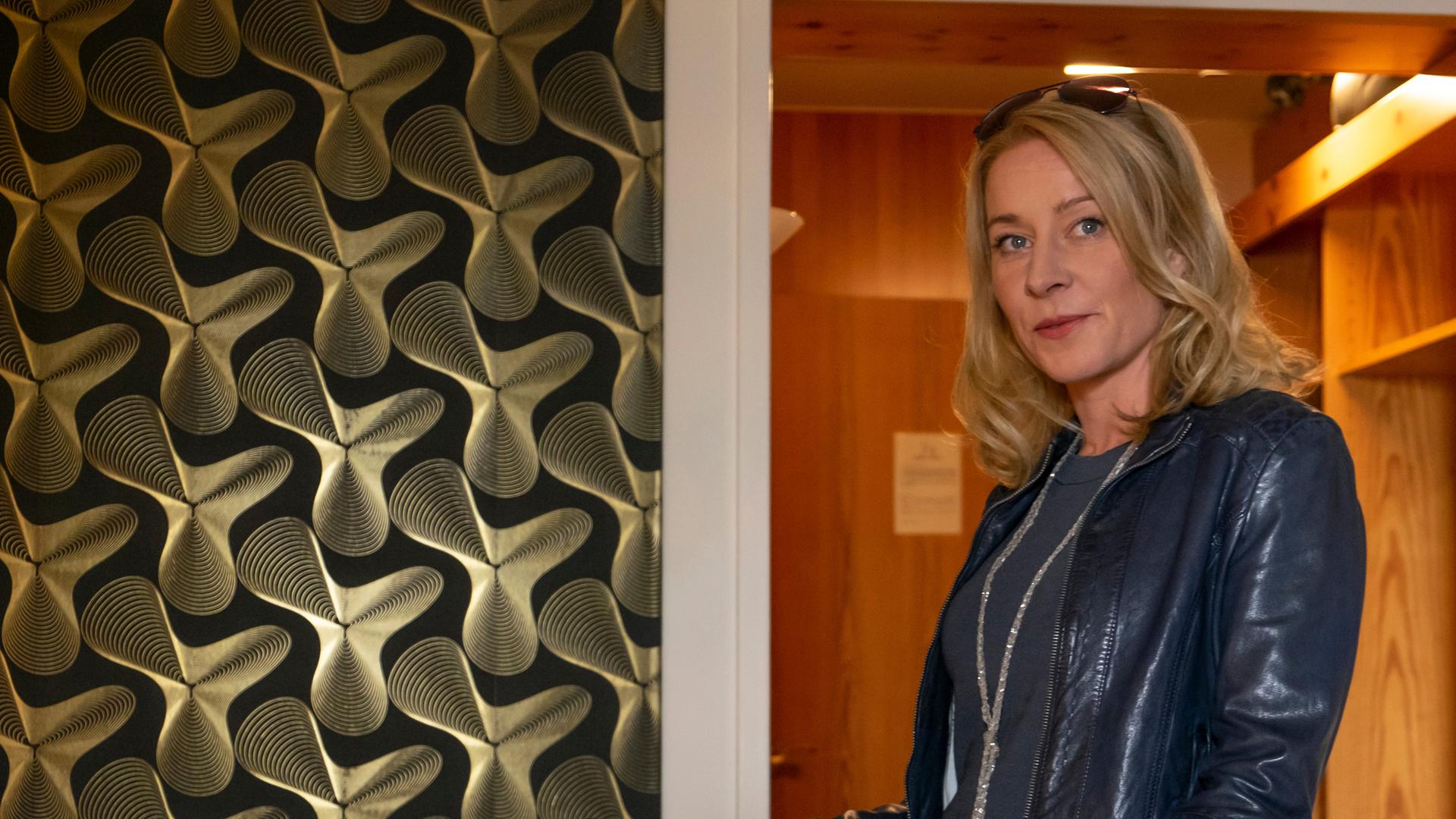 Susanne (Natalie O'Hara) steht im neuen schwarzen Outfit im Hotelzimmer.