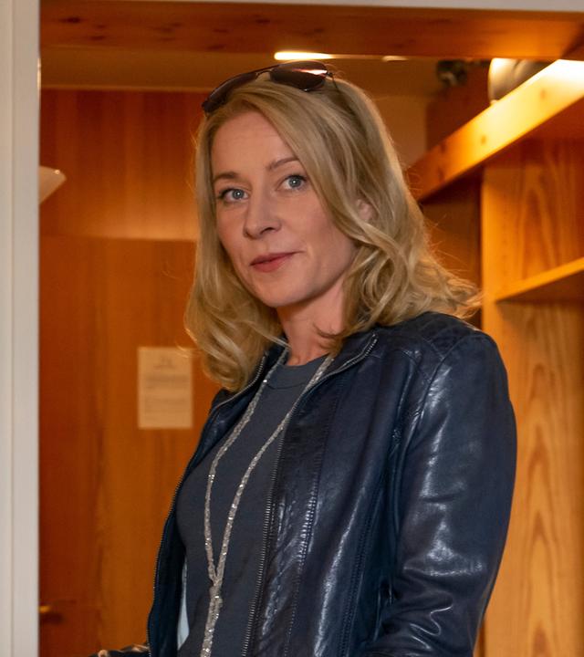 Susanne (Natalie O'Hara) steht im neuen schwarzen Outfit im Hotelzimmer.