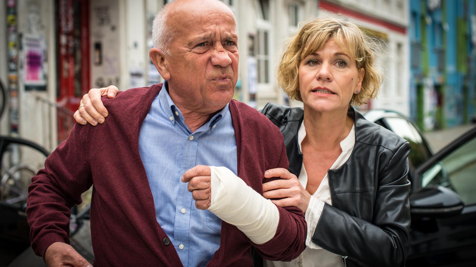 "Notruf Hafenkante - Enkeltrick": Karin Berger (Anne Kasprik) steht neben Erwin Trautmann (Christian Grashof) und hält ihn an Schulter und Arm fest. Der alte Herr hat einen Verband an seiner linken Hand.