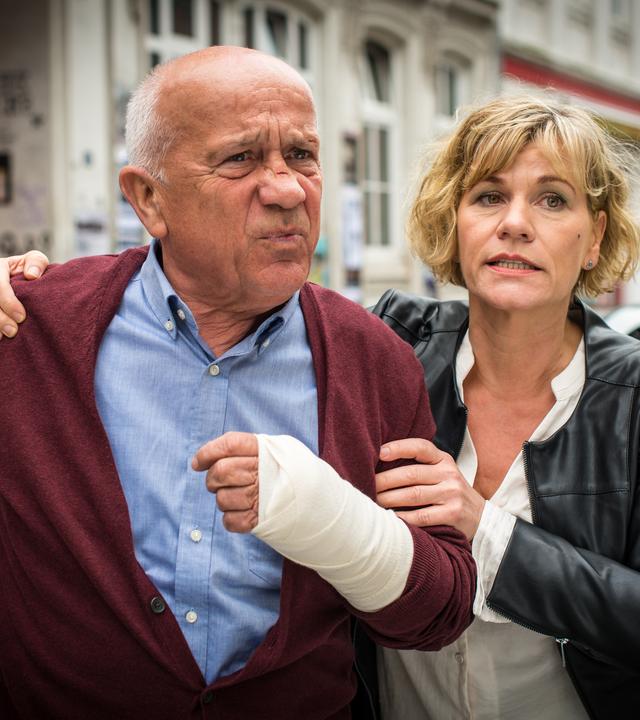 "Notruf Hafenkante - Enkeltrick": Karin Berger (Anne Kasprik) steht neben Erwin Trautmann (Christian Grashof) und hält ihn an Schulter und Arm fest. Der alte Herr hat einen Verband an seiner linken Hand.