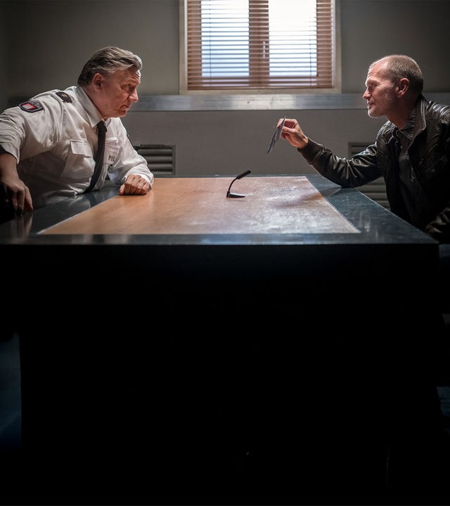 "Notruf Hafenkante - Entführt": Im Befragungsraum sitzen sich Wolf Haller (Hannes Hellmann) und Gregor Ludwig (Michael Witte) an einem Tisch gegenüber und sehen sich an. Ludwig hält ein Foto in seiner rechten Hand, das er Haller zeigt. In der Mitte des Tisches steht ein Mikrofon, das auf Ludwig gerichtet ist.