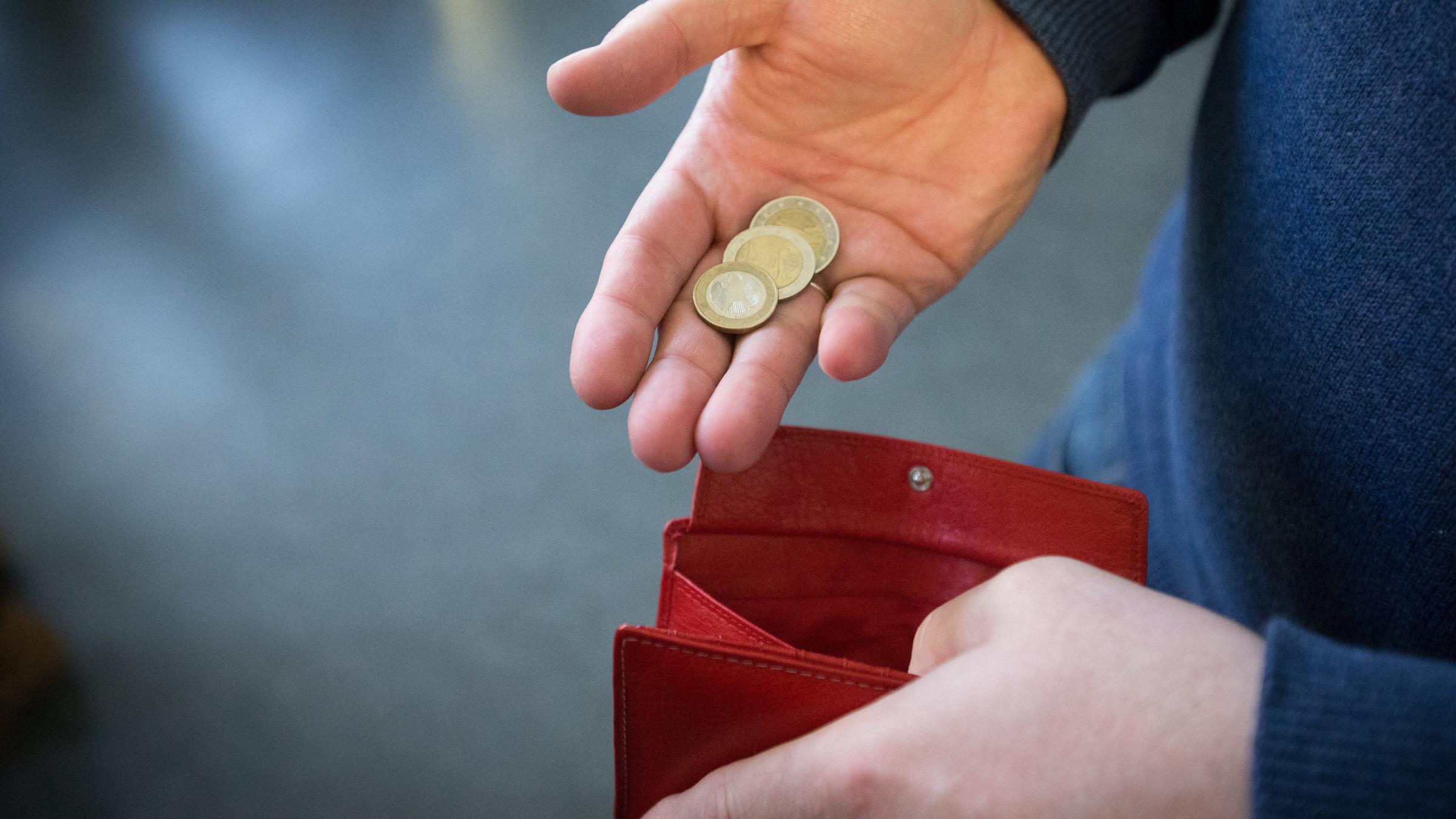 muenzen im wert von fuenf euro werden am 31.01.2017 in paderborn (nordrhein-westfalen) ueber ein rotes portemonnaie gehalten.