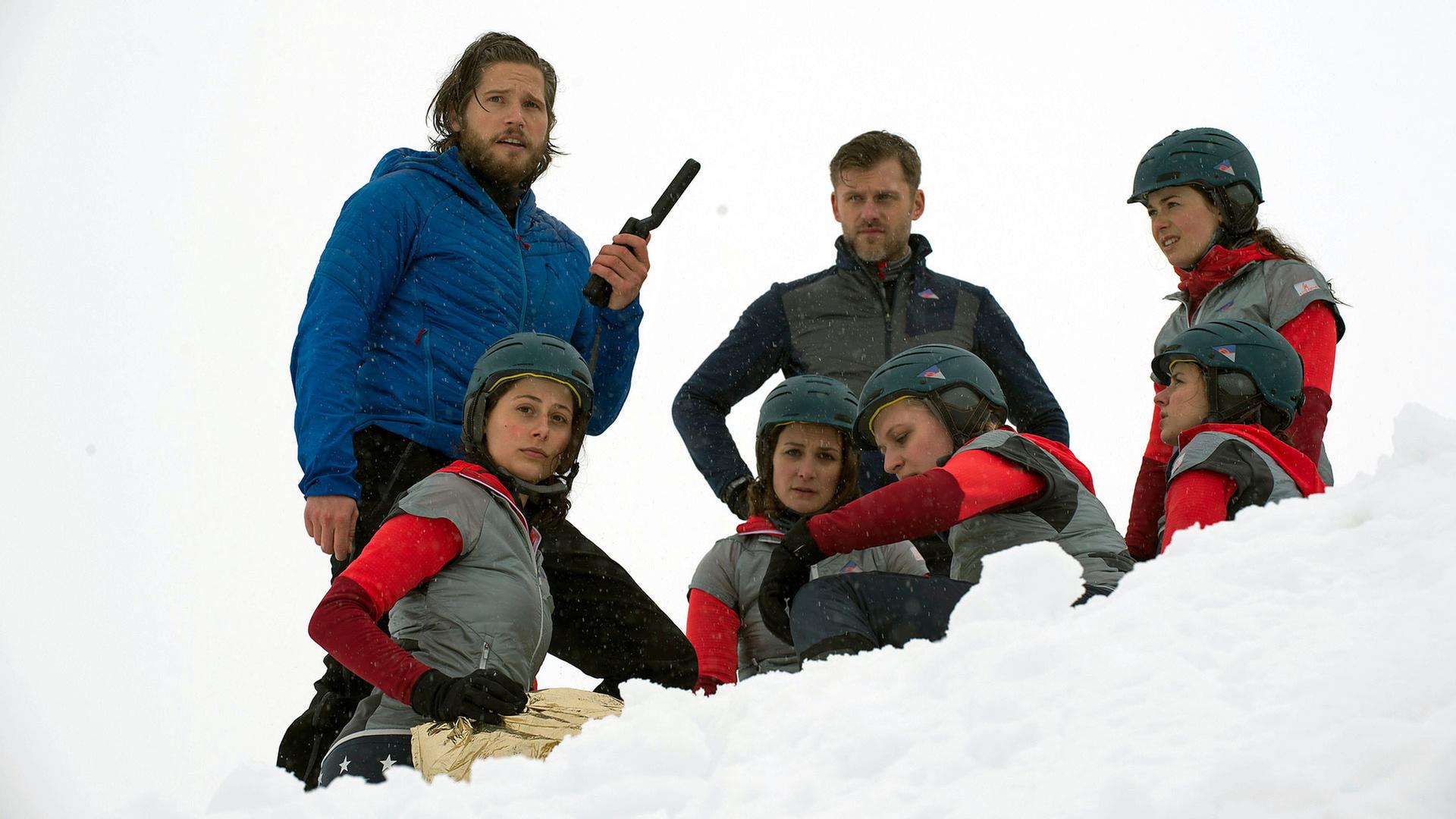 "Die Bergretter: Entscheidung im Eis": Im Schnee liegt Steffi (Laura Cuenca Serrano), eingepackt in eine Rettungsdecke. Daneben stehen Markus (Sebastian Ströbel) mit einem Sprechfunkgerät in der Hand, und Eric (Jens Atzorn). Beide blicken besorgt. Um Steffi herum sitzen Franzi (Julia Eggert), Julia (Diana Ebert), Kathrin (Sandra Maren), Antonia (Julia Schäfle) und Lena (Swantje Riechers) im Schnee.