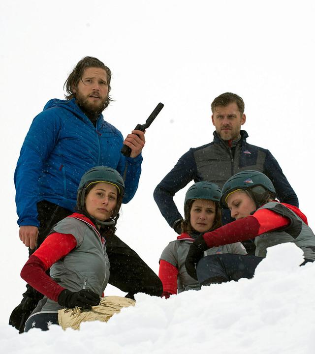 "Die Bergretter: Entscheidung im Eis": Im Schnee liegt Steffi (Laura Cuenca Serrano), eingepackt in eine Rettungsdecke. Daneben stehen Markus (Sebastian Ströbel) mit einem Sprechfunkgerät in der Hand, und Eric (Jens Atzorn). Beide blicken besorgt. Um Steffi herum sitzen Franzi (Julia Eggert), Julia (Diana Ebert), Kathrin (Sandra Maren), Antonia (Julia Schäfle) und Lena (Swantje Riechers) im Schnee.