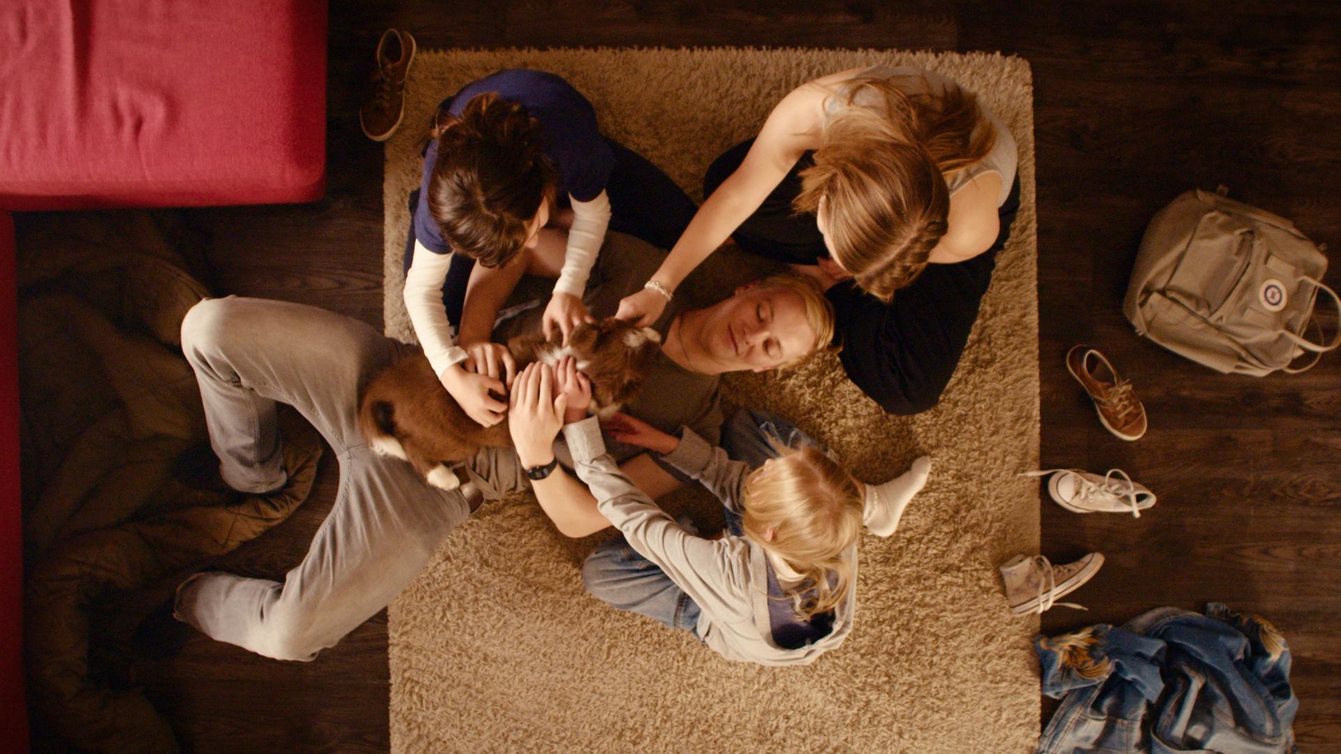 "Gestern waren wir noch Kinder (7)": Daniel Klettmann (Vico Magno), Vivi Klettmann (Julia Beautx) und Emmi Klettmann (Nele Richter) sitzen in einem Kreis. Tim Münzinger (Julius Nitschkoff) liegt in der Mitte mit einem Hund auf dem Bauch, den alle streicheln.