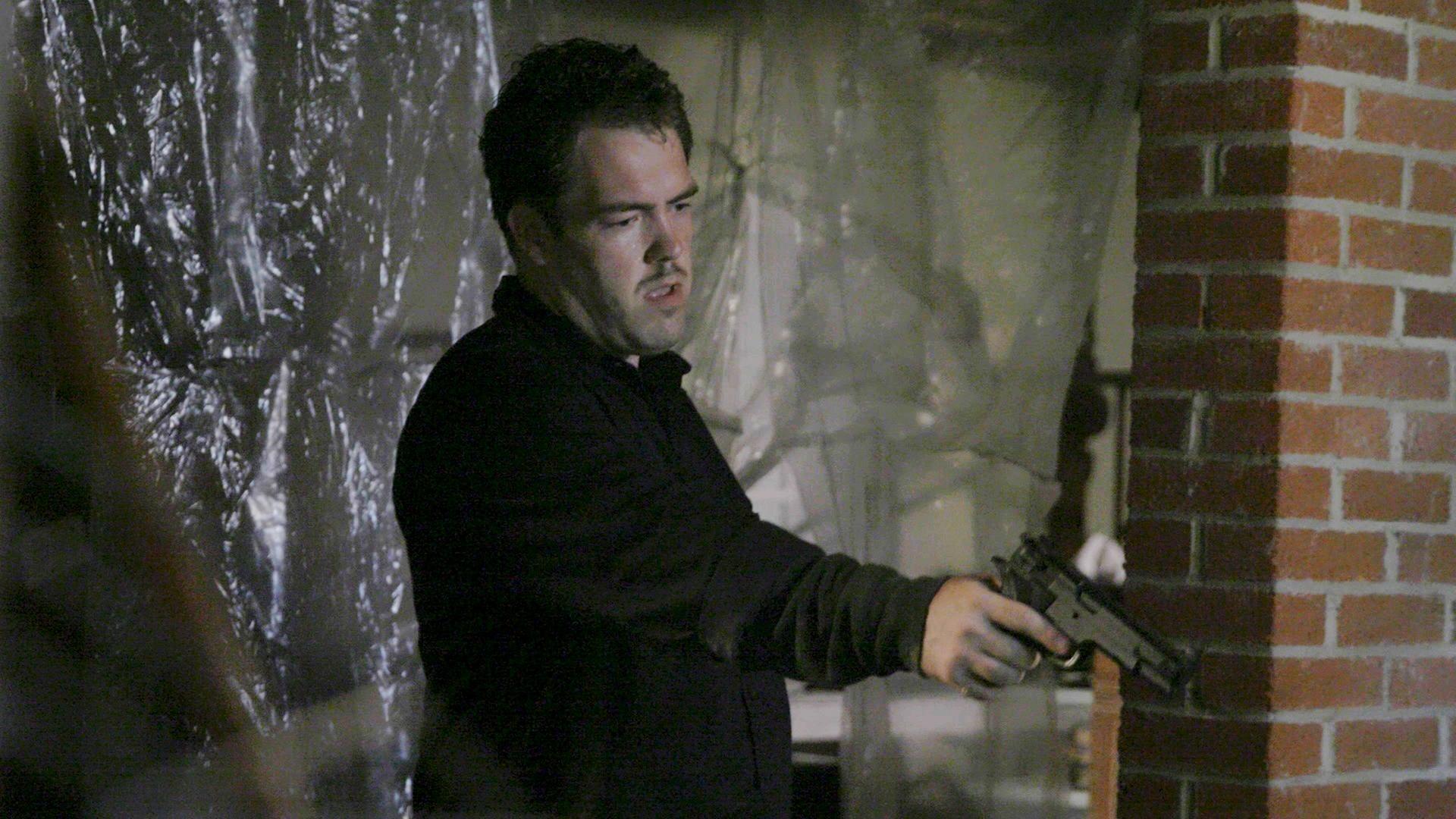 "Erbarmungslos: Israel Keyes - Das fast perfekte Verbrechen": Filmszene: Ein Mann hält eine Pistole in der Hand und zielt nach unten.