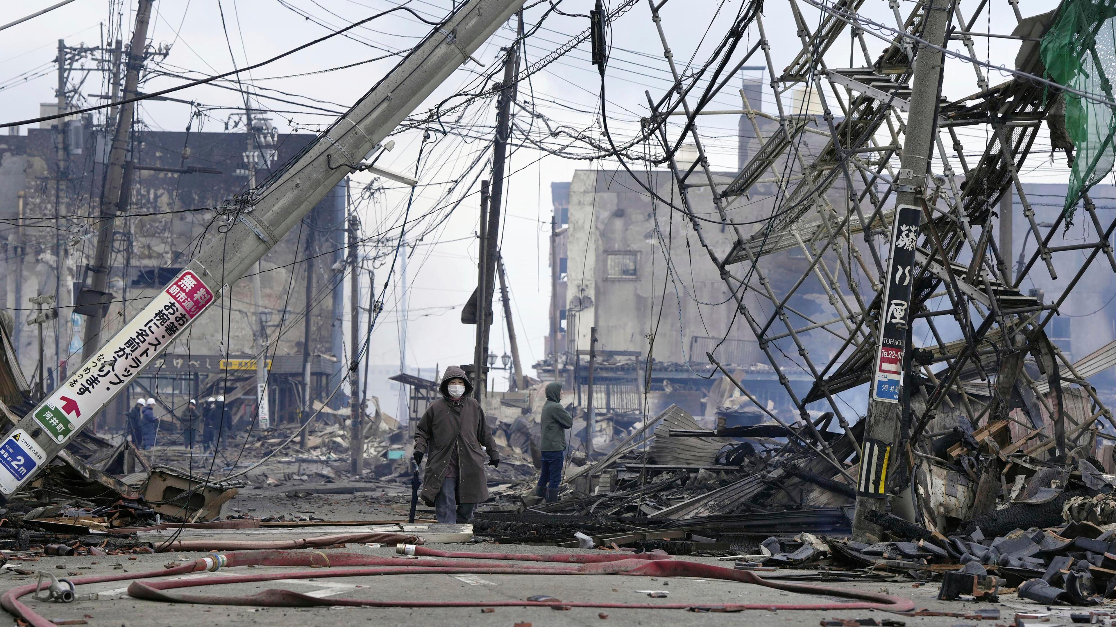 Menschen gehen am 02.01.2024 durch den beschädigten Marktplatz, der nach dem Erdbeben in der Präfektur Ishikawa in Flammen aufgegangen ist