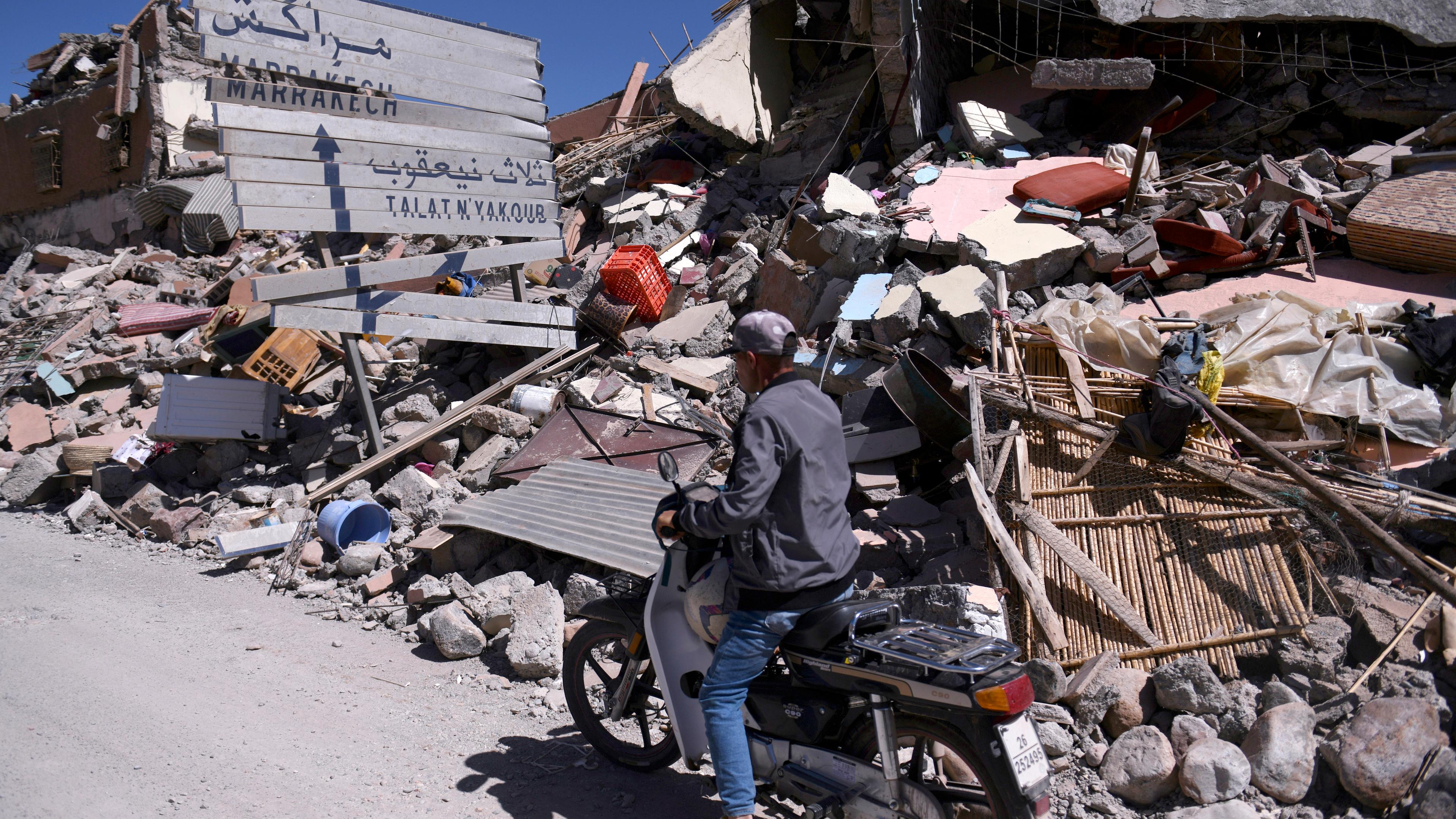 Marokko, Talat N'yakoub: Ein Mann auf einem Motorroller fährt an Trümmern und einem beschädigten Straßenschild vorbei