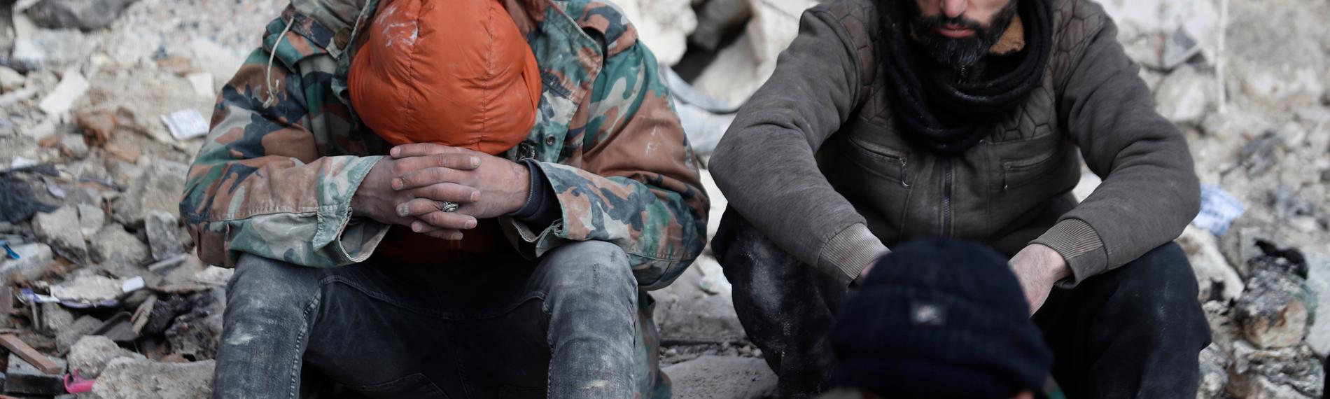 Menschen sitzen auf den Trümmern eingestürzter Gebäude in Aleppo