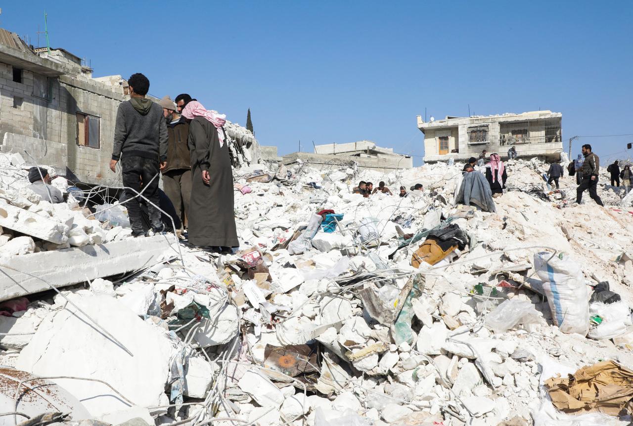 Menschen stehen auf Trümmern mehrere Gebäude, die infolge der Erdbeben-Katastrophe im türkisch-syrischen Grenzgebiet zerstört worden sind.