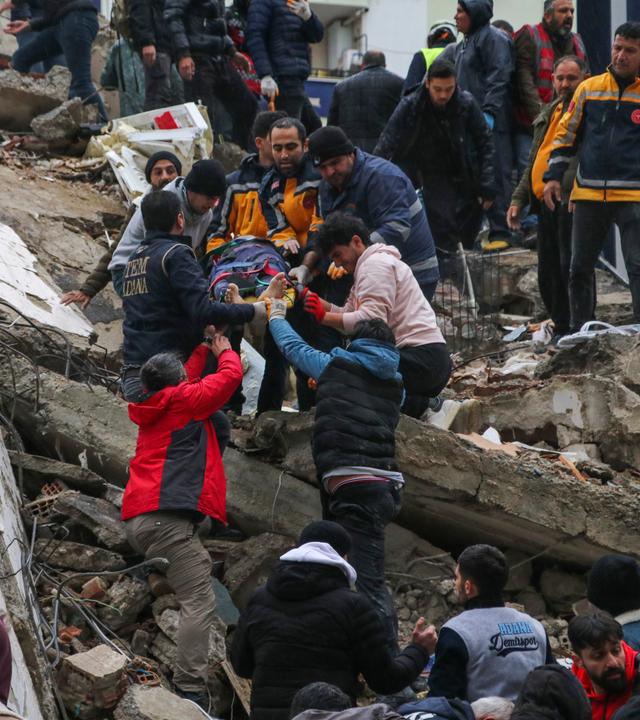 Zu sehen sind Helfer, die Verletze aus den Trümmern eines Hauses bergen. 