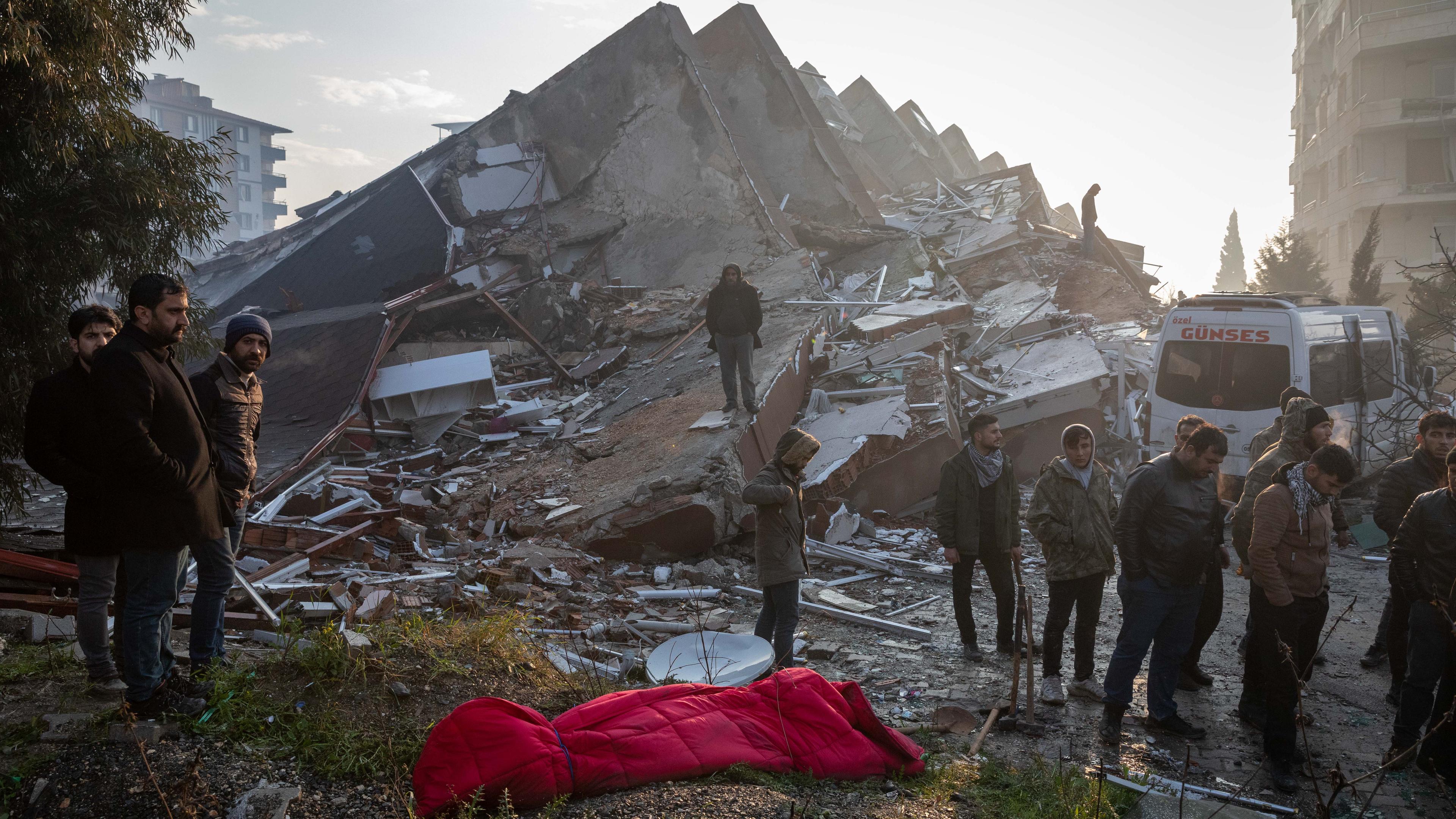 Türkei, Antakya: Menschen stehen vor einem Gebäude das nach einem Erbeben in Trümmern steht.