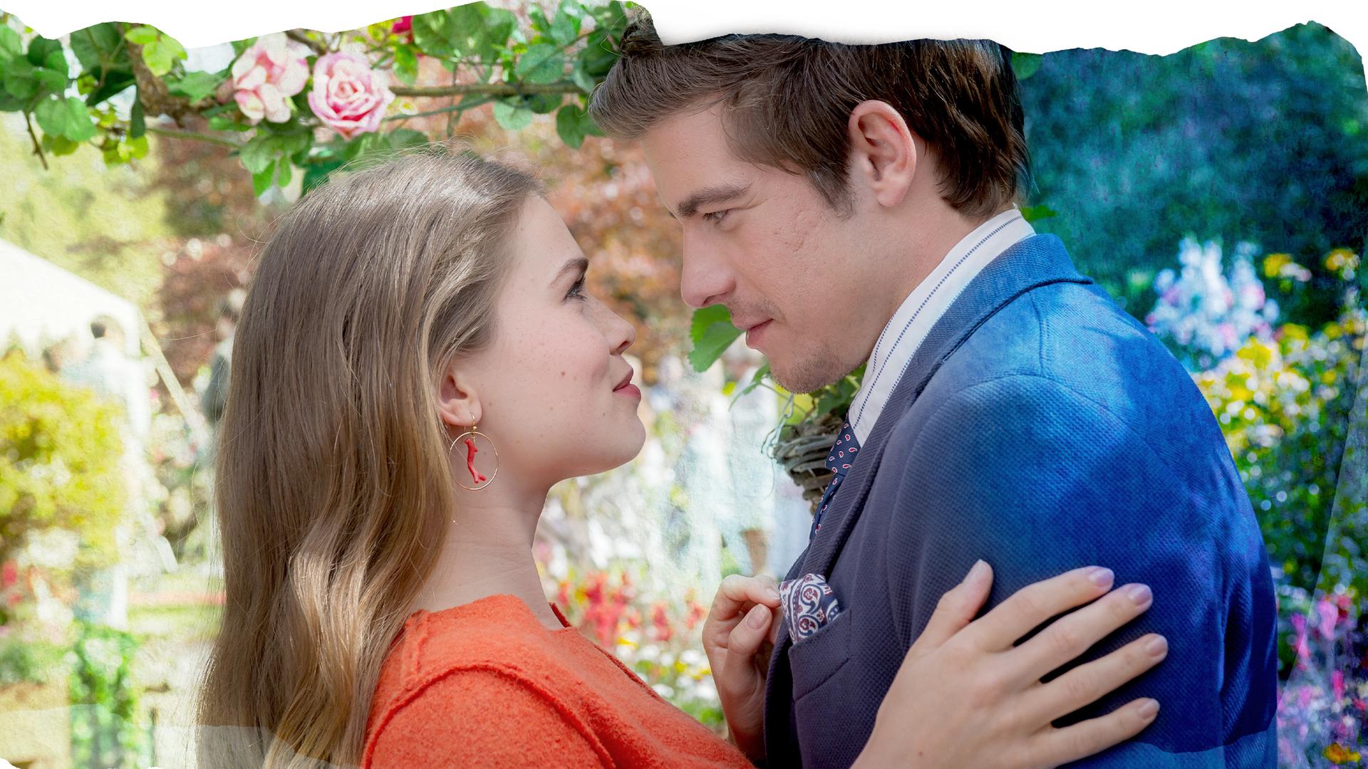 "Rosamunde Pilcher - Erdbeeren im Frühling": Inmitten von Blumen stehen Lilly (Zoe Moore) und Nicholas (Philipp Danne) eng umschlungen und schauen sich verliebt in die Augen.