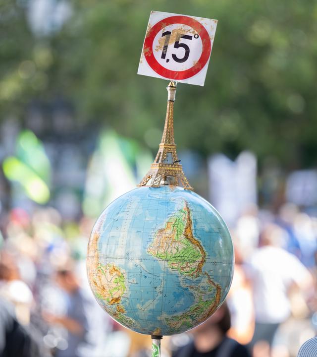 Auf einer Demo wird ein Globus mit einem Eifelturm und einem Schild mit der Aufschrift "1,5 Grad" hochgehalten.