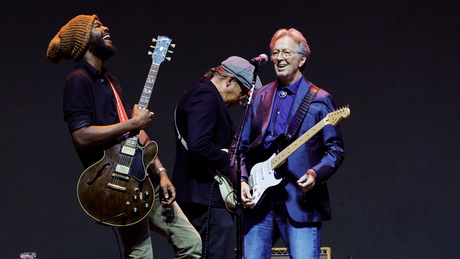 Eric Clapton steht mit seiner Gitarre und einem weiteren Musiker mit Gitarre auf der Bühne.