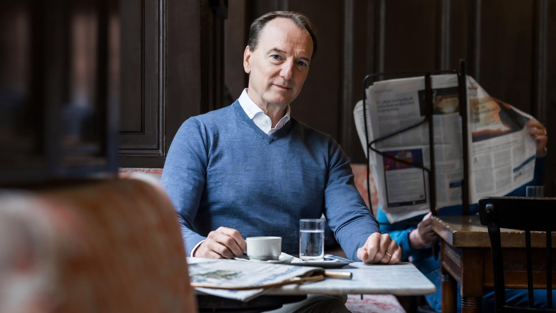 Ein Mann sitzt in einem Cafe und blickt in Richtung Kamera