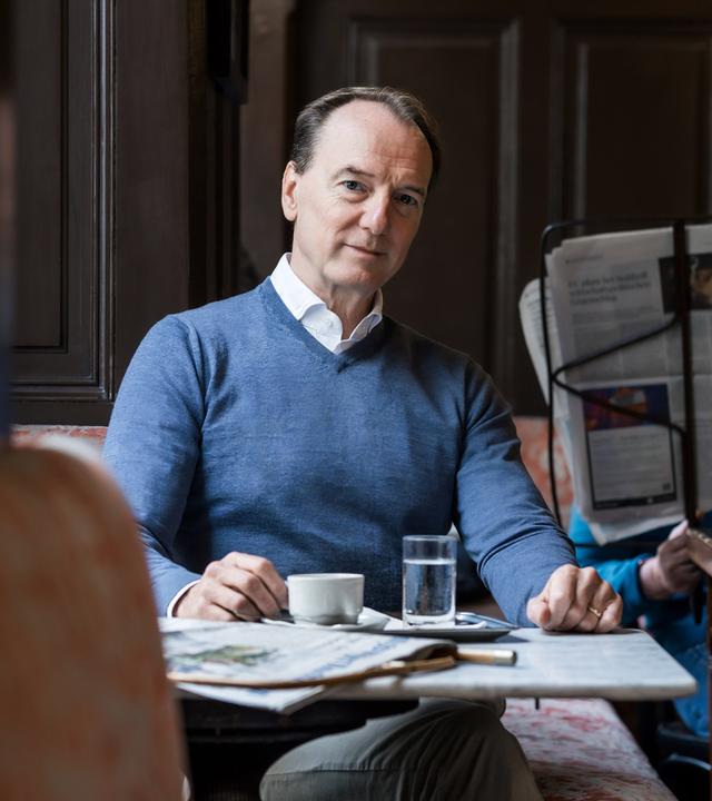 Ein Mann sitzt in einem Cafe und blickt in Richtung Kamera