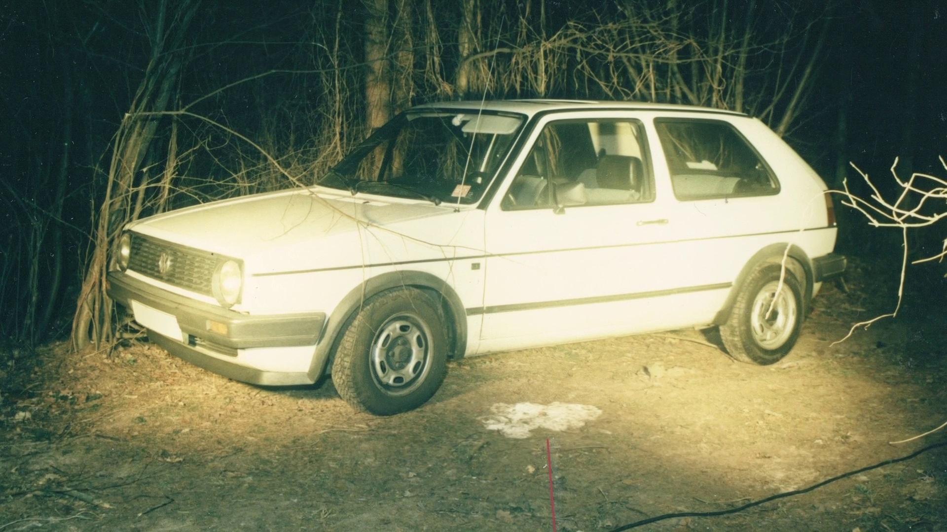 "Ermittler! - Lückenlose Indizienkette": Original Tatort-Foto eines weißen VW Golf auf einem dunklen Waldweg.