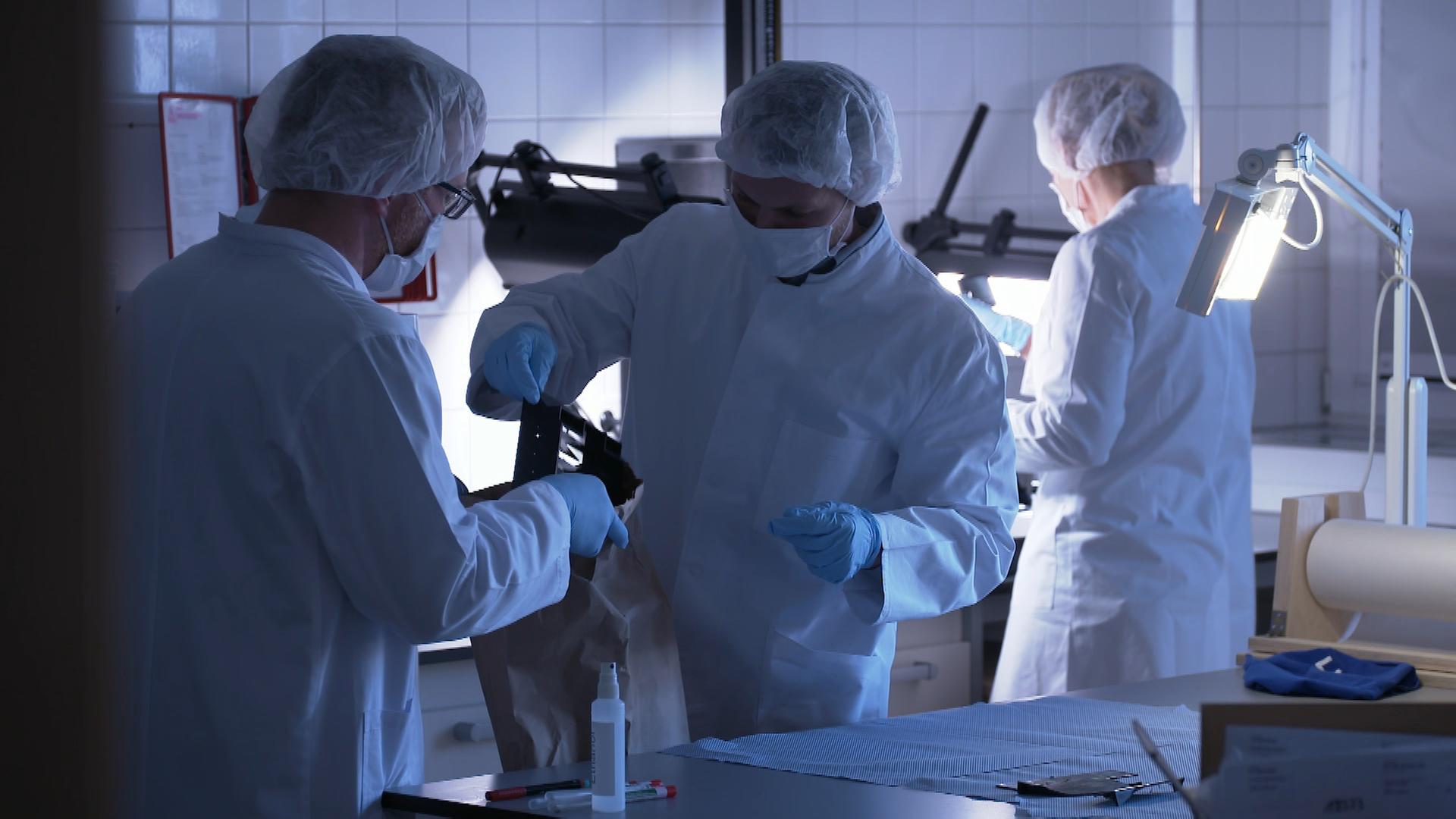 "Ermittler! Bis zum Äußersten": Drei Menschen in weißer Schutzkleidung arbeiten in einem Labor.